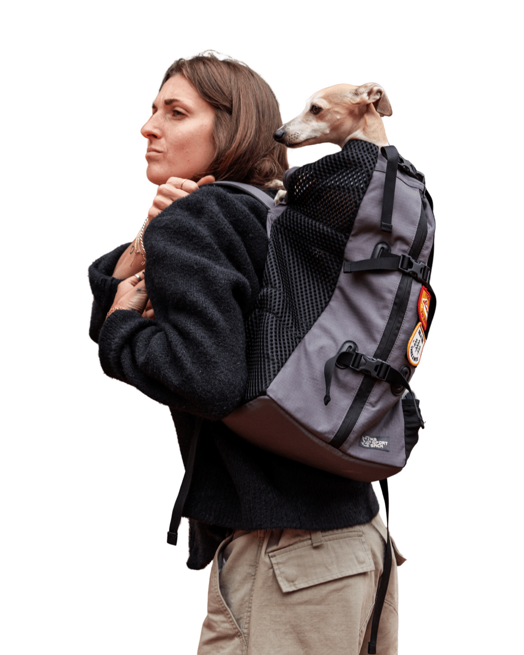 A woman wearing a gray and black dog backpack carrier with a small dog sitting inside, shown from the side against a plain white background.