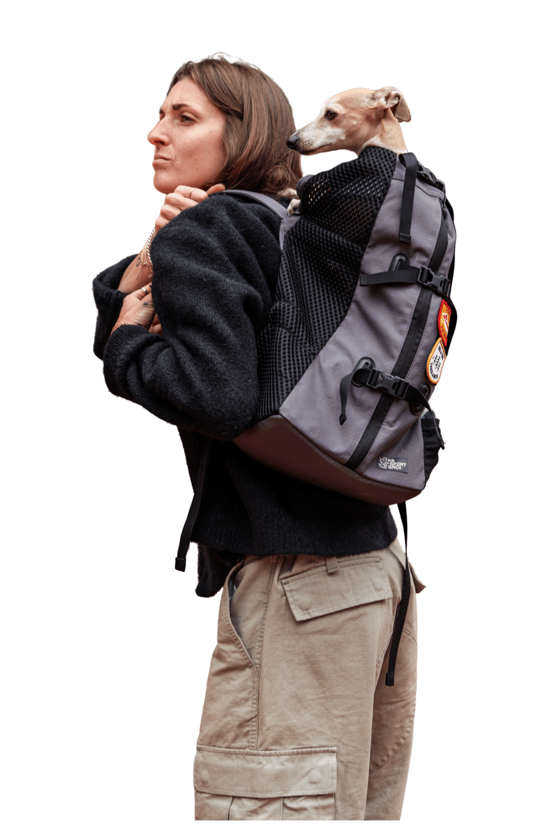 A woman wearing a gray and black dog backpack carrier with a small dog sitting inside, shown from the side against a plain white background.