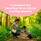 A woman crouches on a forest path interacting with a dog, with a pink text banner at the top reading 'Convenient and mess-free for on-the-go training sessions.'.